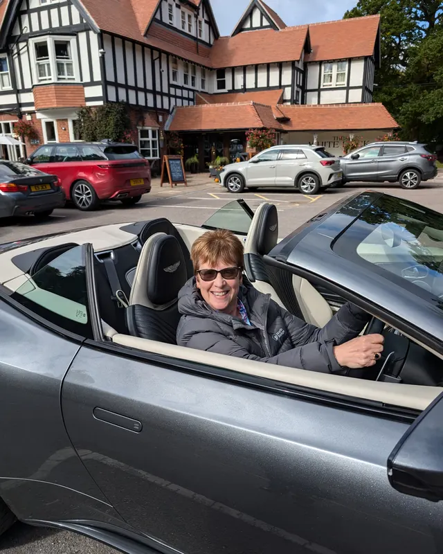 A customer smiling in an Aston Martin DB11 Volante with the roof down