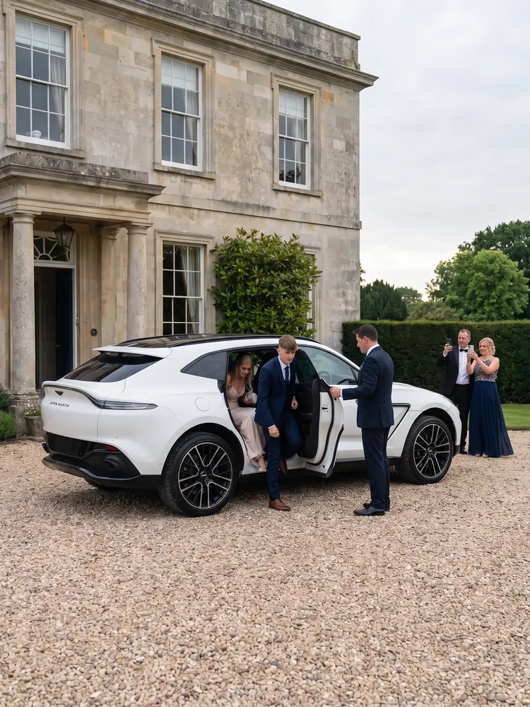 Prom-goers stepping out of a white Aston Martin DBX 707 at a country hotel