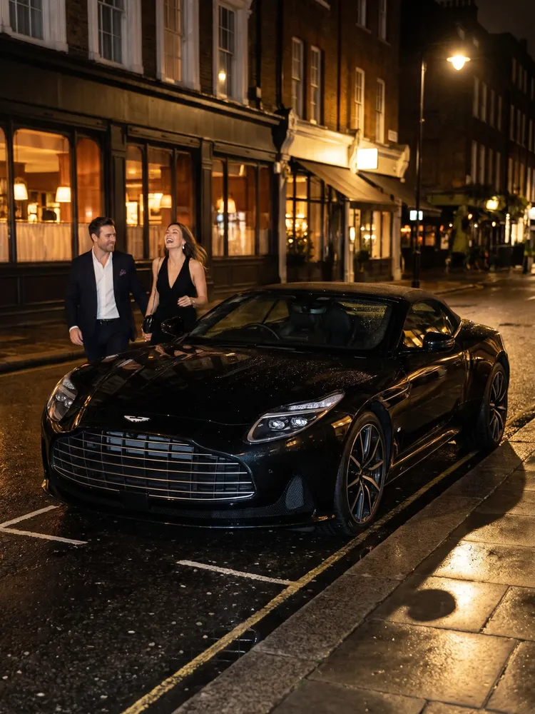 A couple walking to a black Aston Martin DB12 outside a restaurant at night