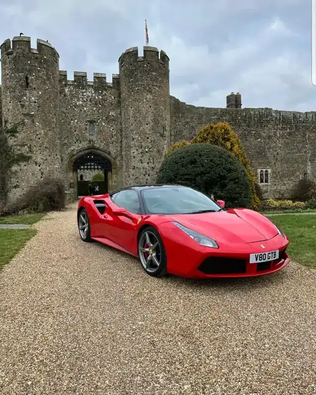Red Ferrari 488 parked in front of a castle gatehouse