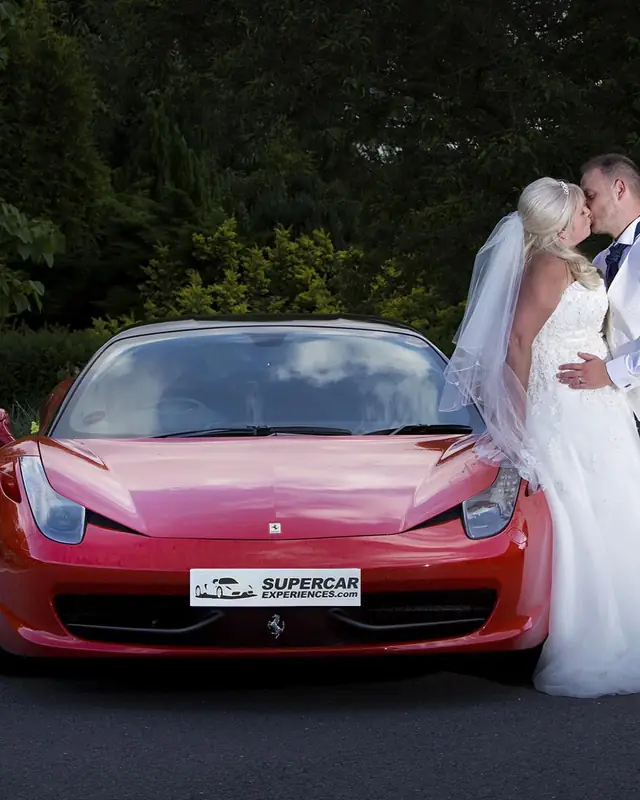 A bride and groom kissing in front of a red Ferrari on their wedding day