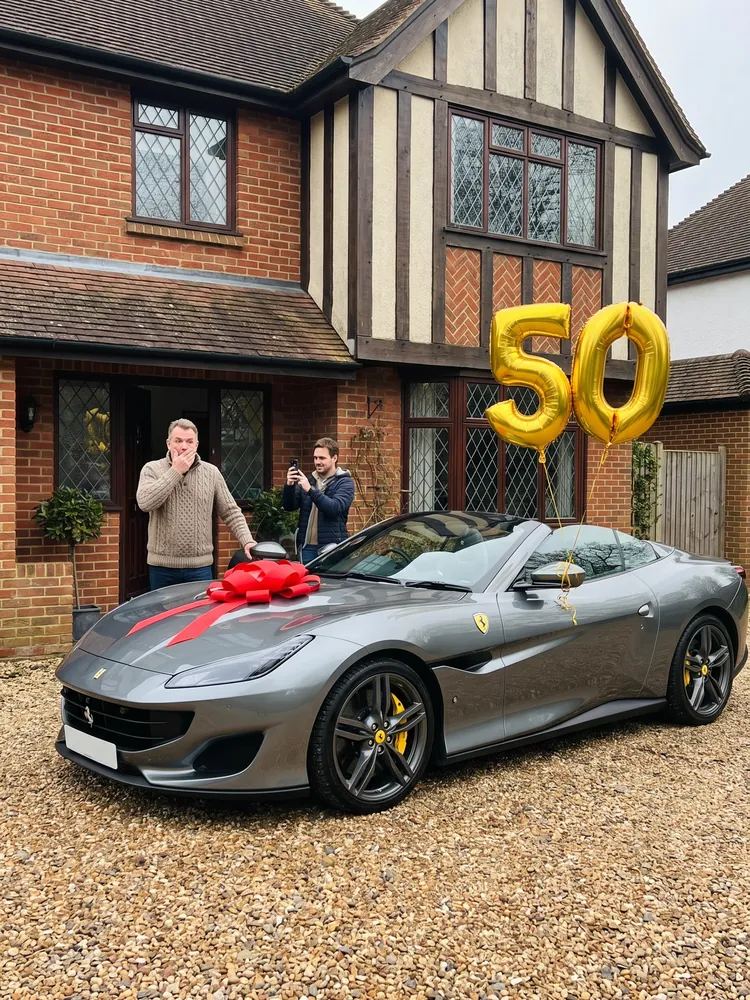 A grey Ferrari Portofino M with a bow and 50 balloons on a driveway