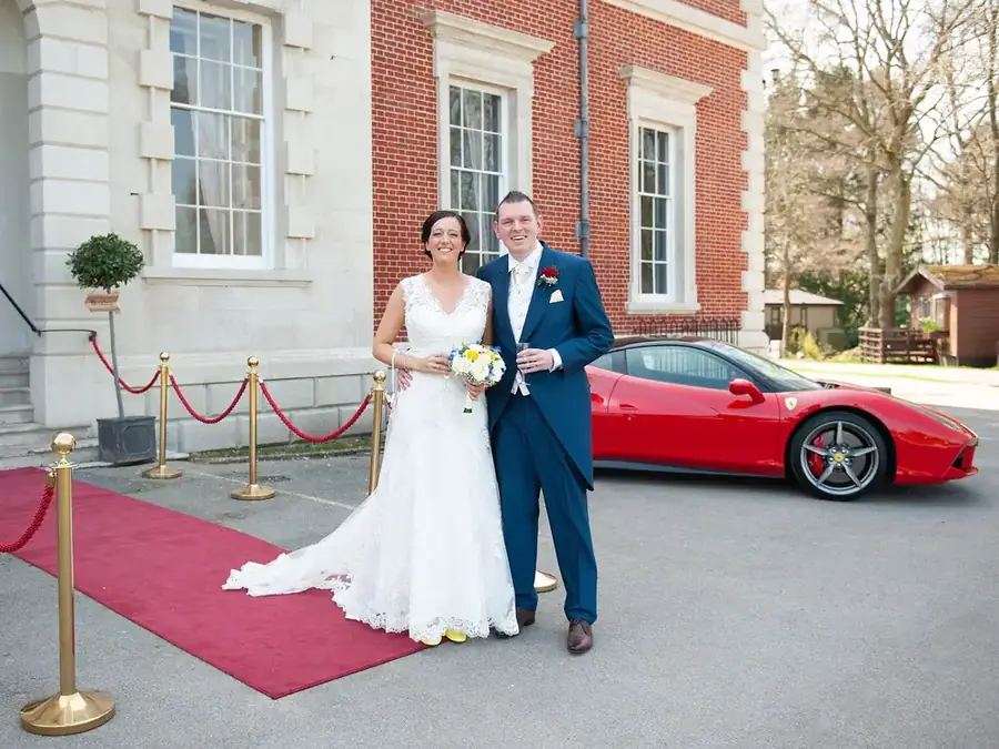 Bride and groom on a red carpet with a red Ferrari 488 behind them
