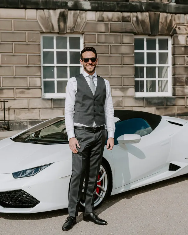 A man in a waistcoat beside a white Lamborghini Huracán Spyder
