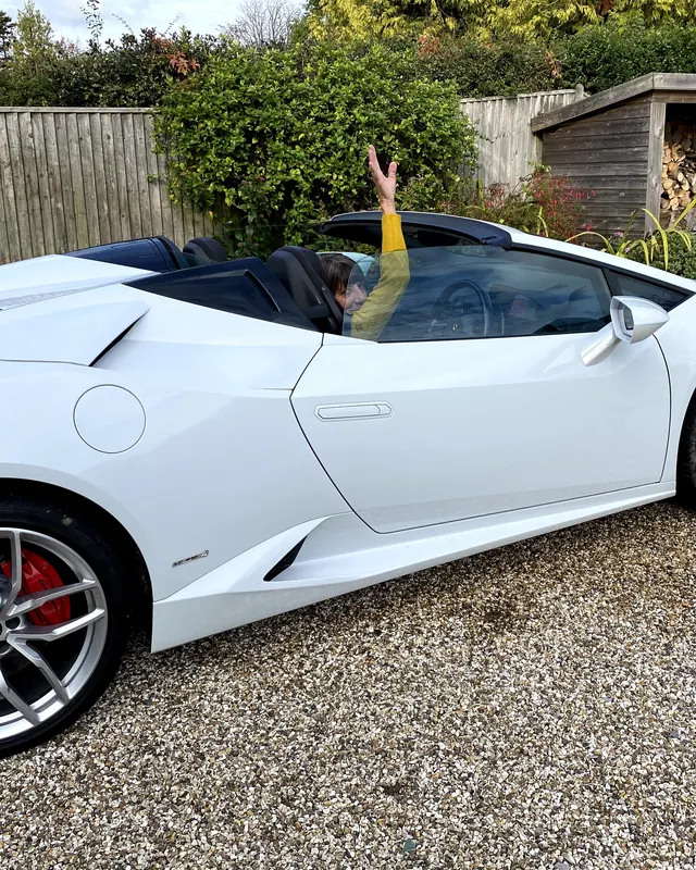 A woman waving from a white Lamborghini Huracán, an anniversary gift