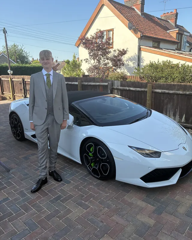 A young man in a suit beside a white Lamborghini on his prom night