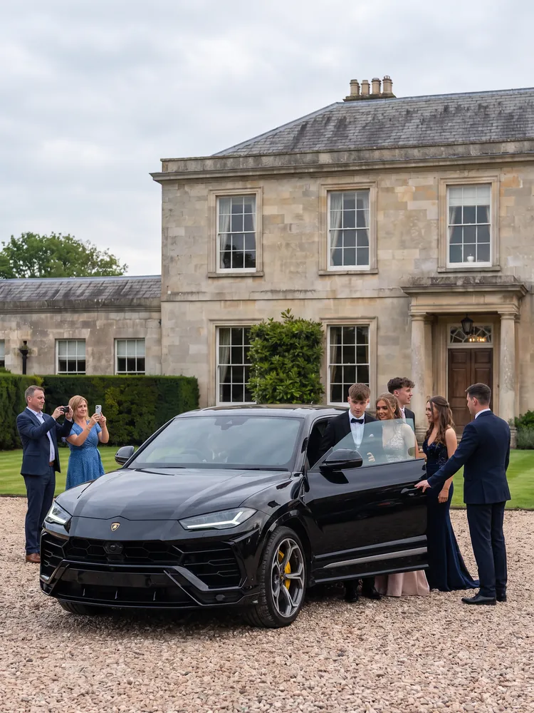 Prom-goers climbing out of a black Lamborghini Urus at a country hotel