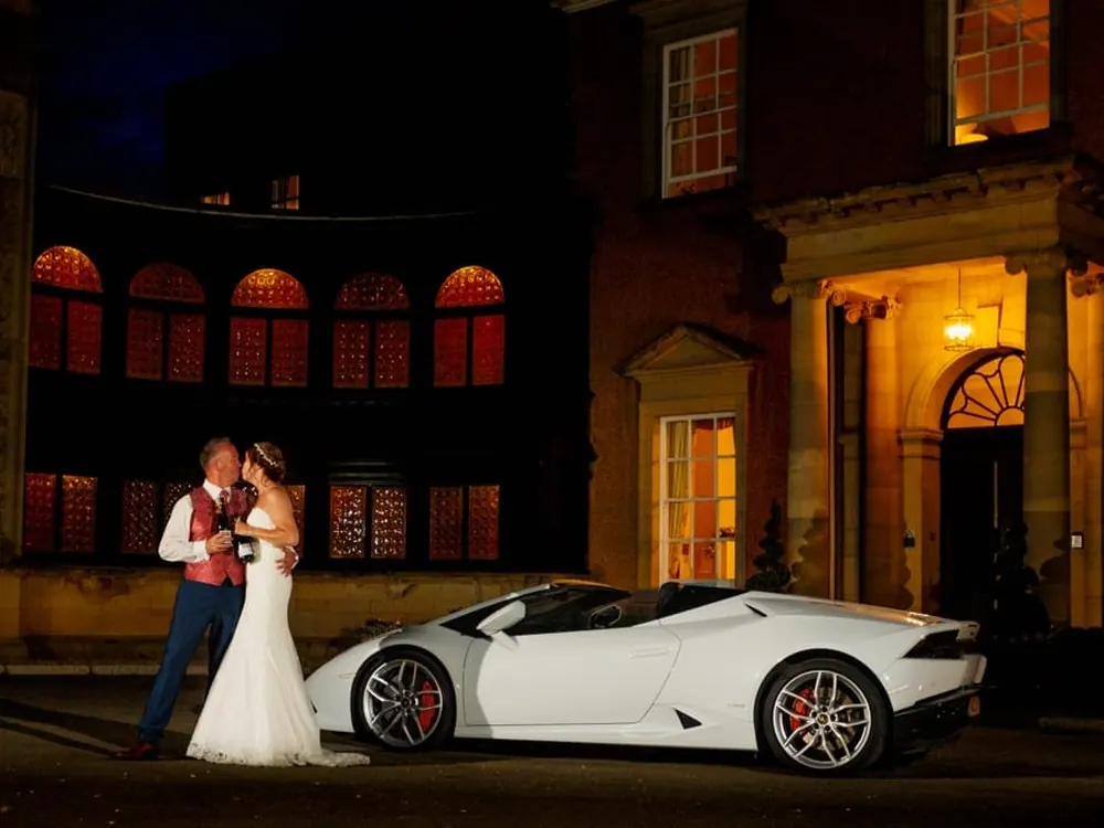 A bride and groom beside a white Lamborghini Huracán at night