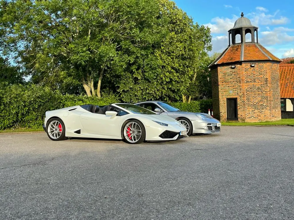 Two supercars parked by a dovecote on a weekend away