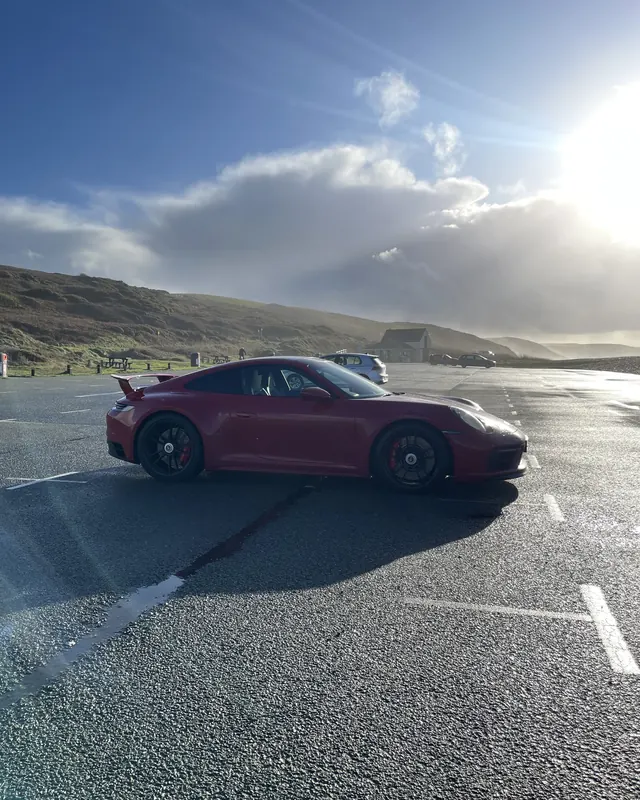 Red Porsche 911 GTS on a coastal car park, a surprise from his wife