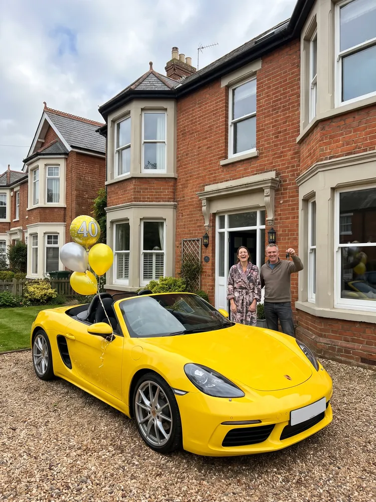 A yellow Porsche Boxster with birthday balloons on a driveway