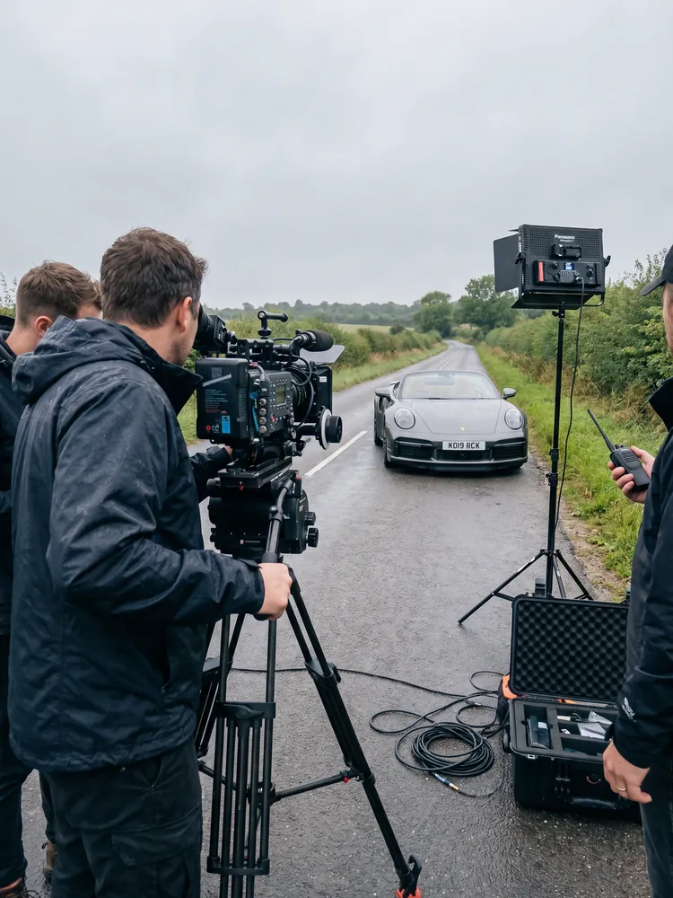 A film crew shooting a silver Porsche 911 Turbo S Cabriolet on a country road