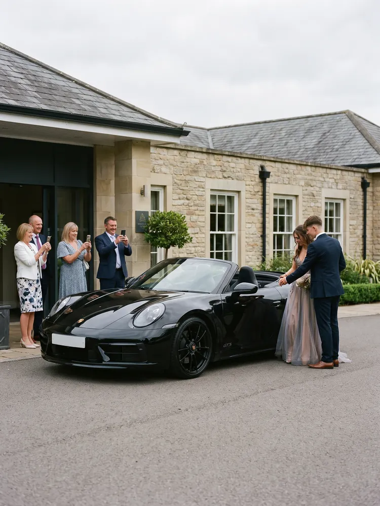 A black Porsche 911 GTS Cabriolet arriving at a hotel for a school prom